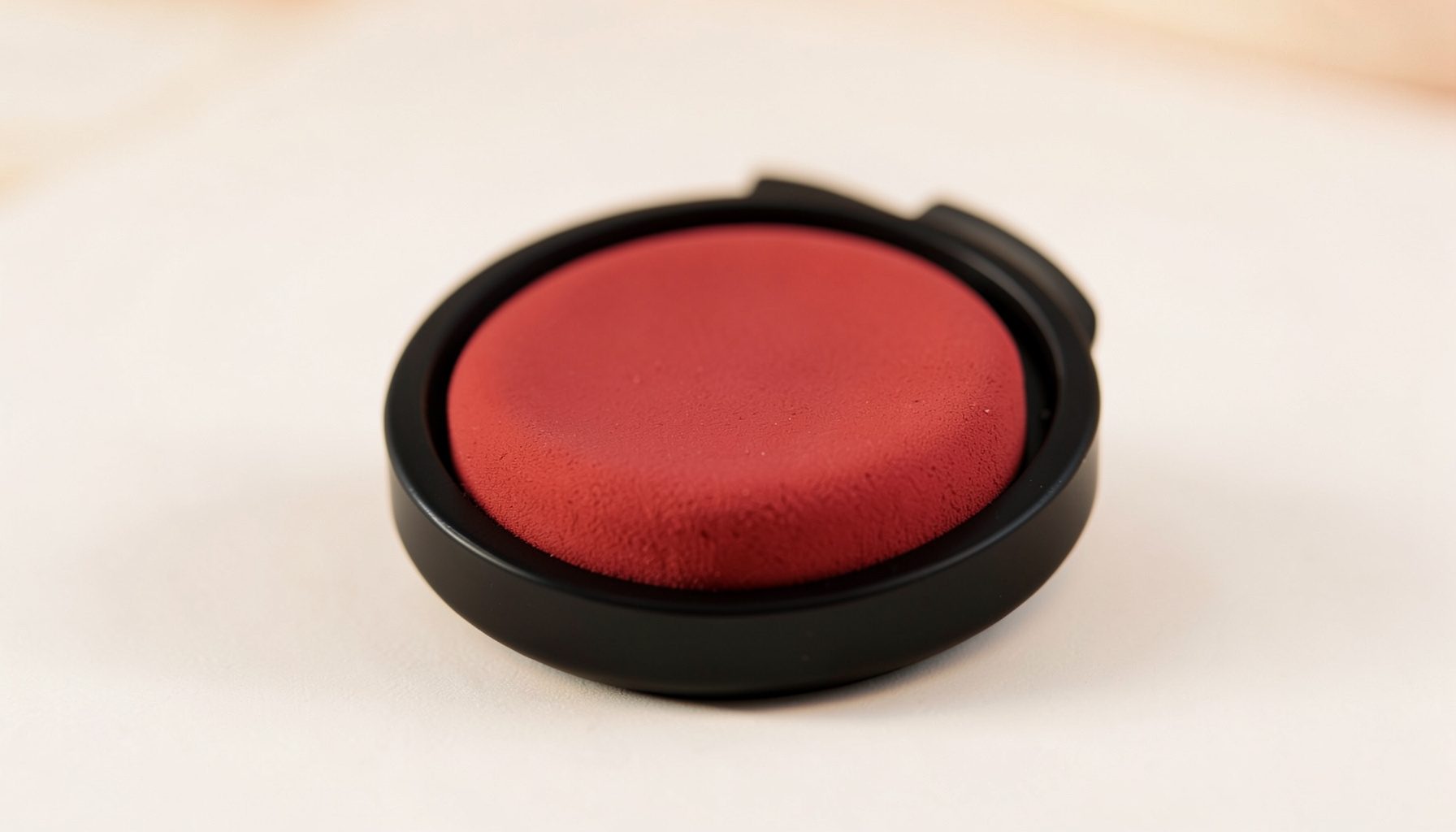 Primer plano de una base de maquillaje en formato cushion compacto negro con esponja, sobre una superficie clara con tonos suaves.